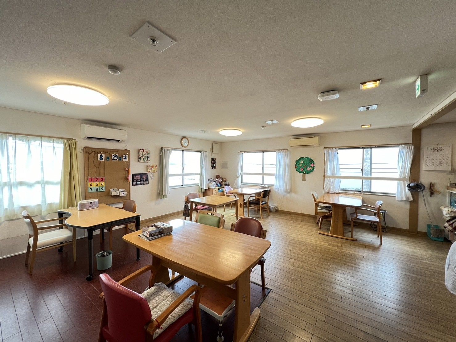 緑の多い屋外の遊歩道で散策を楽しんでいる眼鏡をかけている高齢女性と付き添いの女性スタッフ。高齢女性は車いすを利用している。