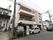 薄いピンク色を基調とした３階建ての施設。１階には接骨院があり、２階、３階部分にはベランダが設置されている。