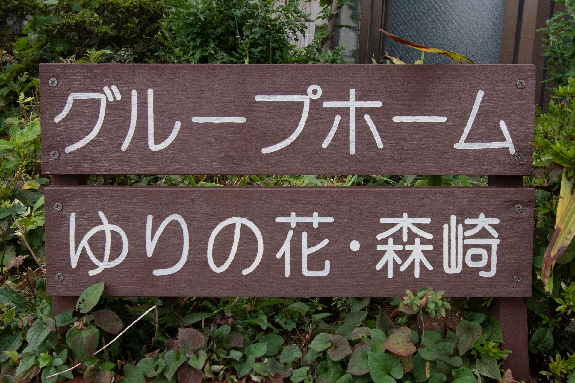 草の中に配置されたグループホームゆりの花・森崎と書かれた木製の看板