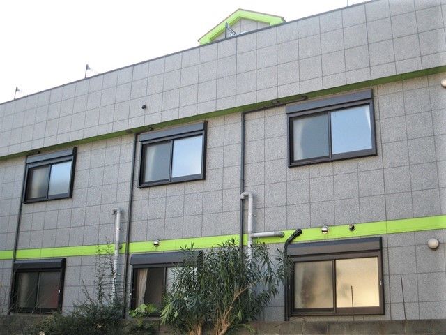 グレーのどっしりとした建物。２階建てで周りには木がたくさん植えられている。