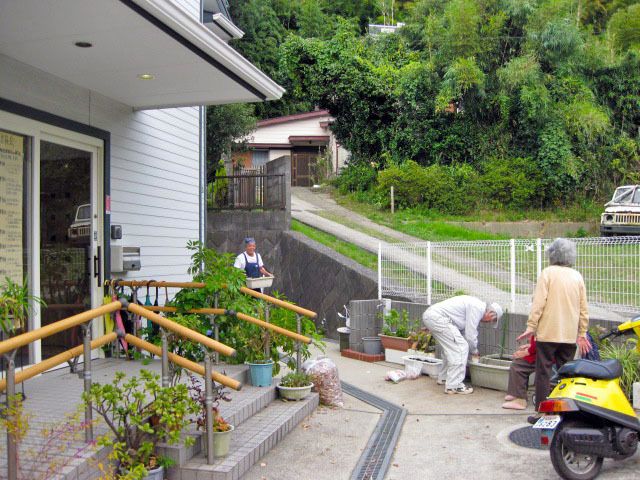 施設の玄関で庭いじりをしている高齢者の様子。周辺の自然豊かな環境が分かる写真