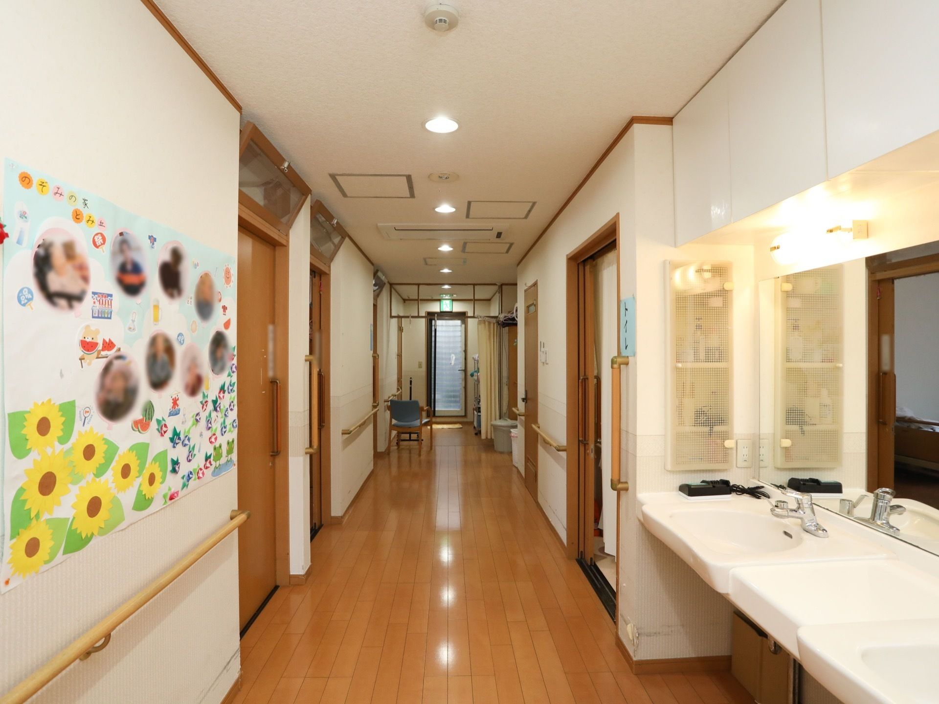 通路の途中に鏡付きの洗面台が設置されている。洗面台の向かい側の壁に入居者様の写真をコラージュした作品が掲示されている。