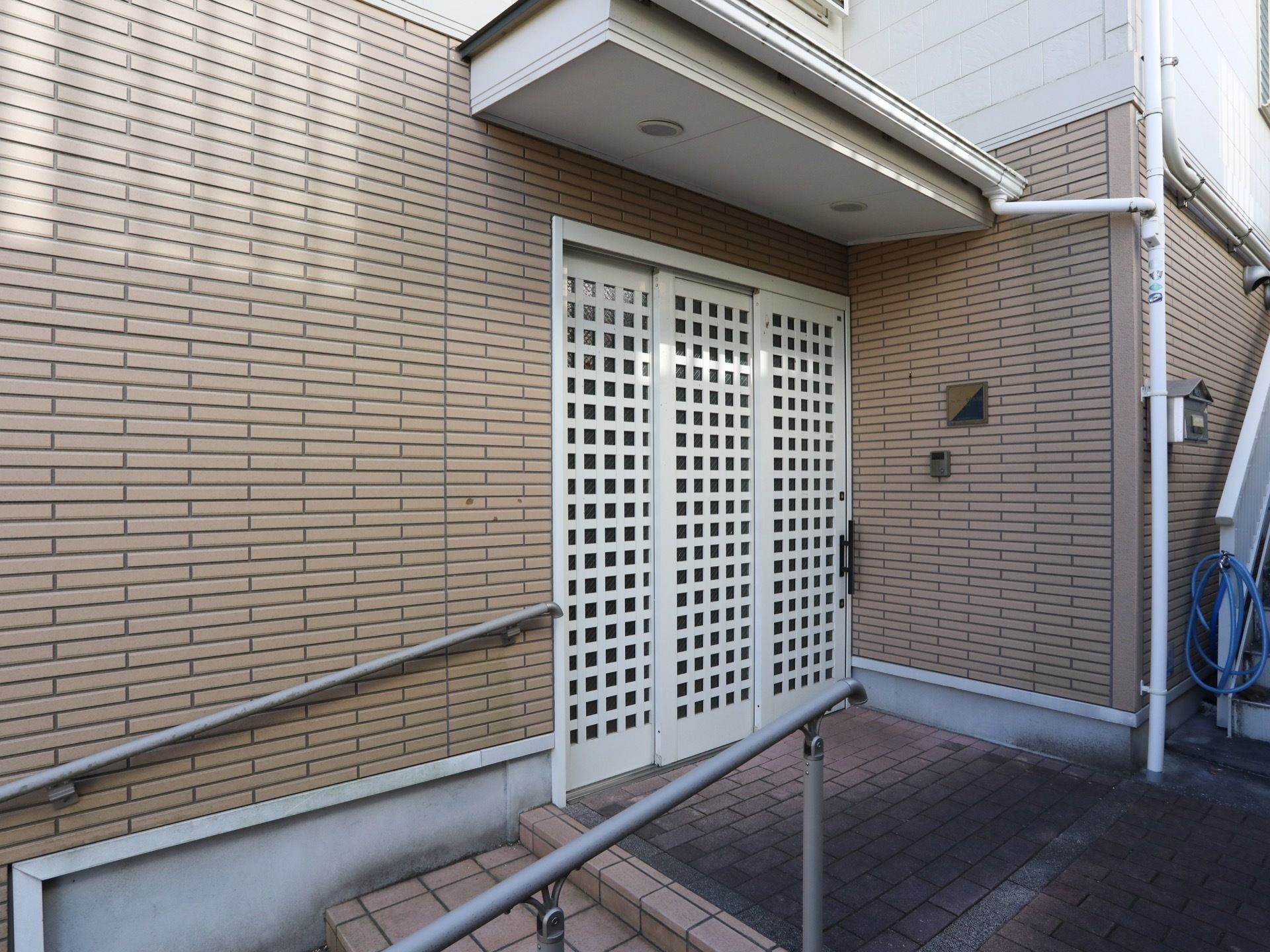 玄関横にスロープがあり、玄関のドアの上に屋根がつけられている。ドアの横にインターフォンが設置されている。