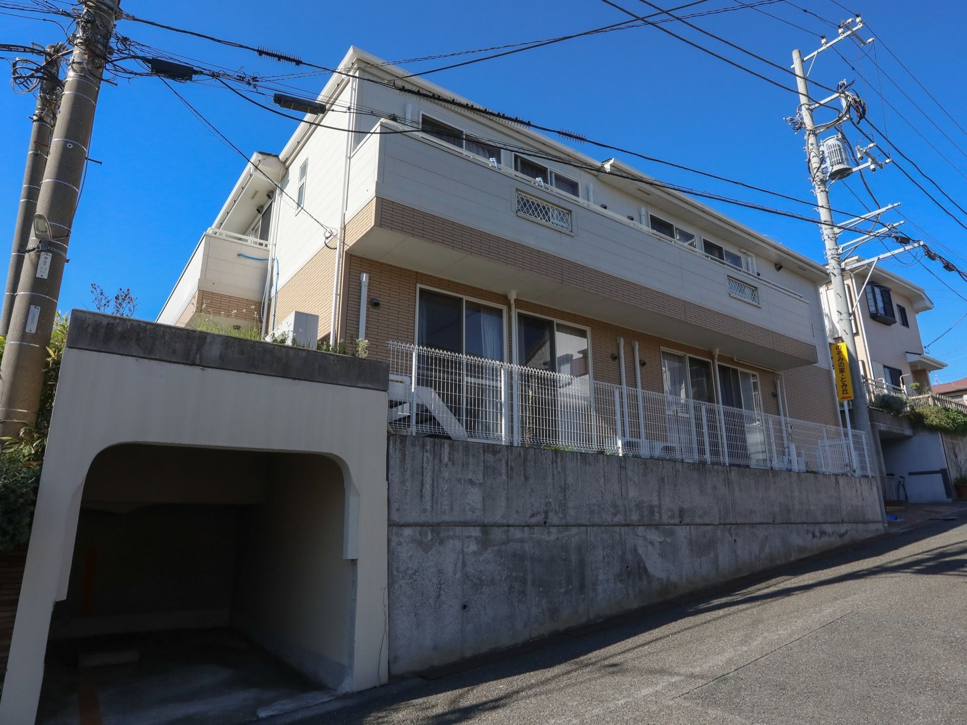 ベージュと白を基調とした２階建ての施設。坂道の途中の高台に建てられ、施設の周囲は白い柵で囲まれている。