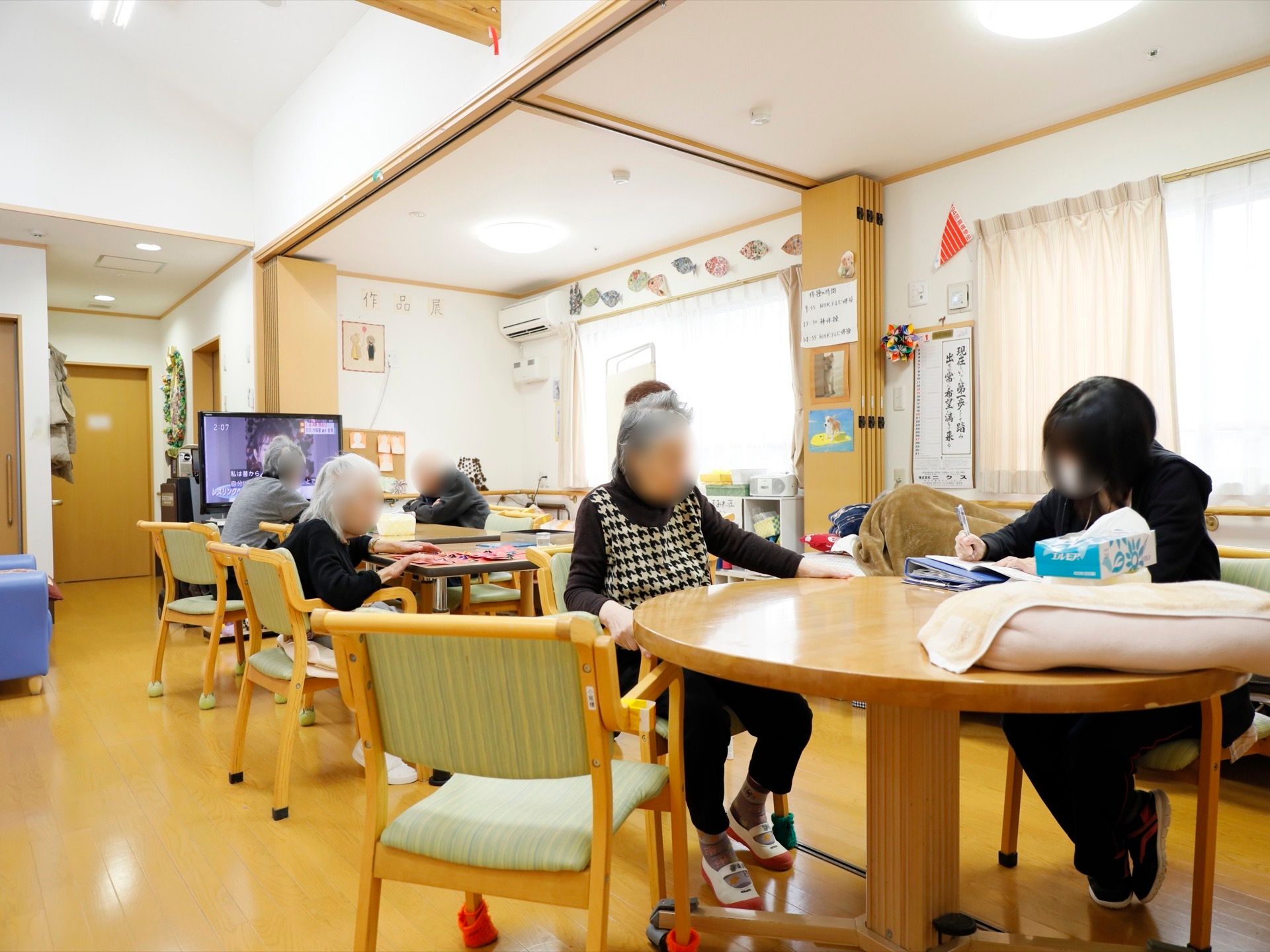 薄いピンクのカーテンがかけられた、大きな窓が２つあり、部屋には可動式の壁が設置されている。また、エアコンが１台取りつけられている。