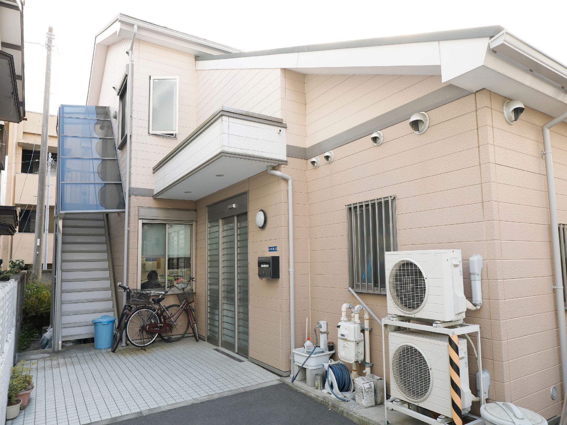 2階に直接上がる階段に、雨除けの屋根がついている施設の外観