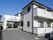 白色を基調とした外壁の２階建ての施設である。各居室にバルコニーがある。玄関前に車寄せがあり、車が停まっている。