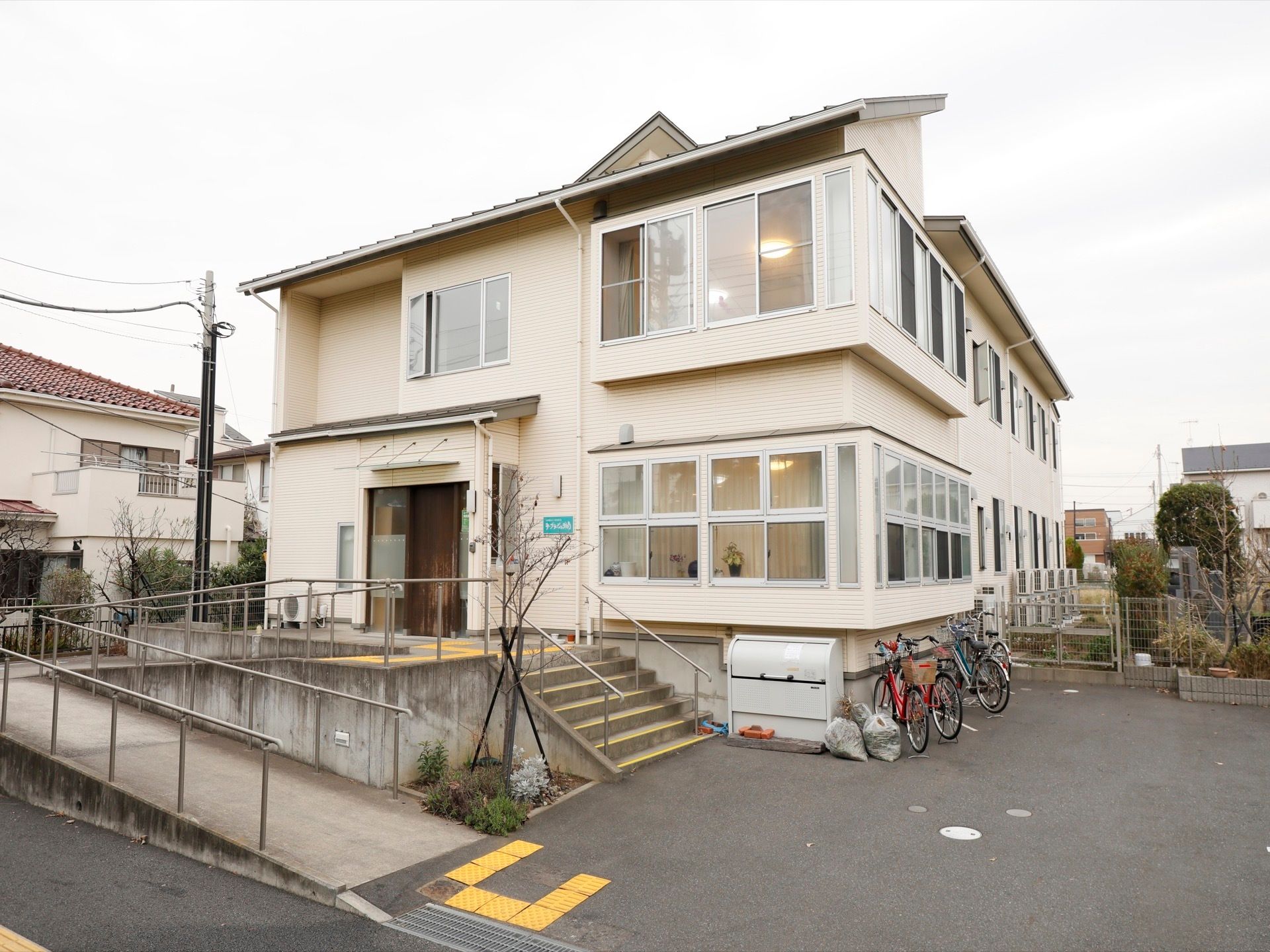 ２階建ての建物で、敷地内には駐輪場やごみ箱が設置されている。玄関前には手すりのついた階段とスロープがある。