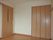 大きなクローゼットが付いたフローリングの部屋には引き戸が付き、ドアのそばにはグリーンのボタンがある。