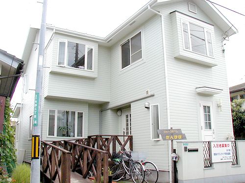 白を基調とした２階建ての建物は玄関から手すり付きのスロープが伸びていて、駐輪場もある。