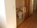 居室の出入口からすぐの所にトイレを備えている。横側にスライド式の木目調のドアを設けている。外側の壁に照明のスイッチがある。