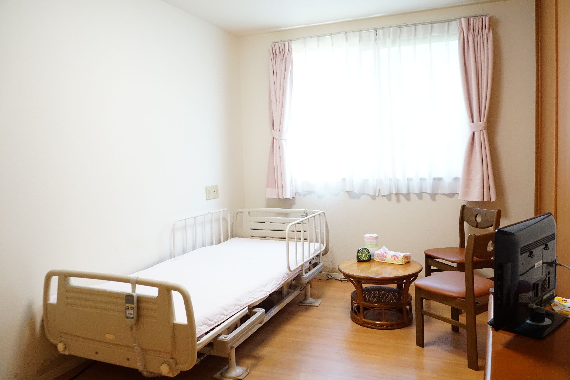 窓から光が降り注ぎ、介護ベッド、椅子、テーブルが置かれている居室