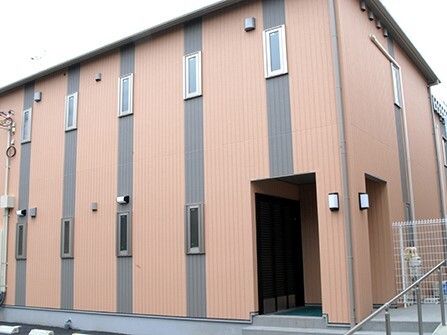 ブラウン系の２階建ての建物は玄関先には手すり付きのスロープと階段があり、窓が少ない。