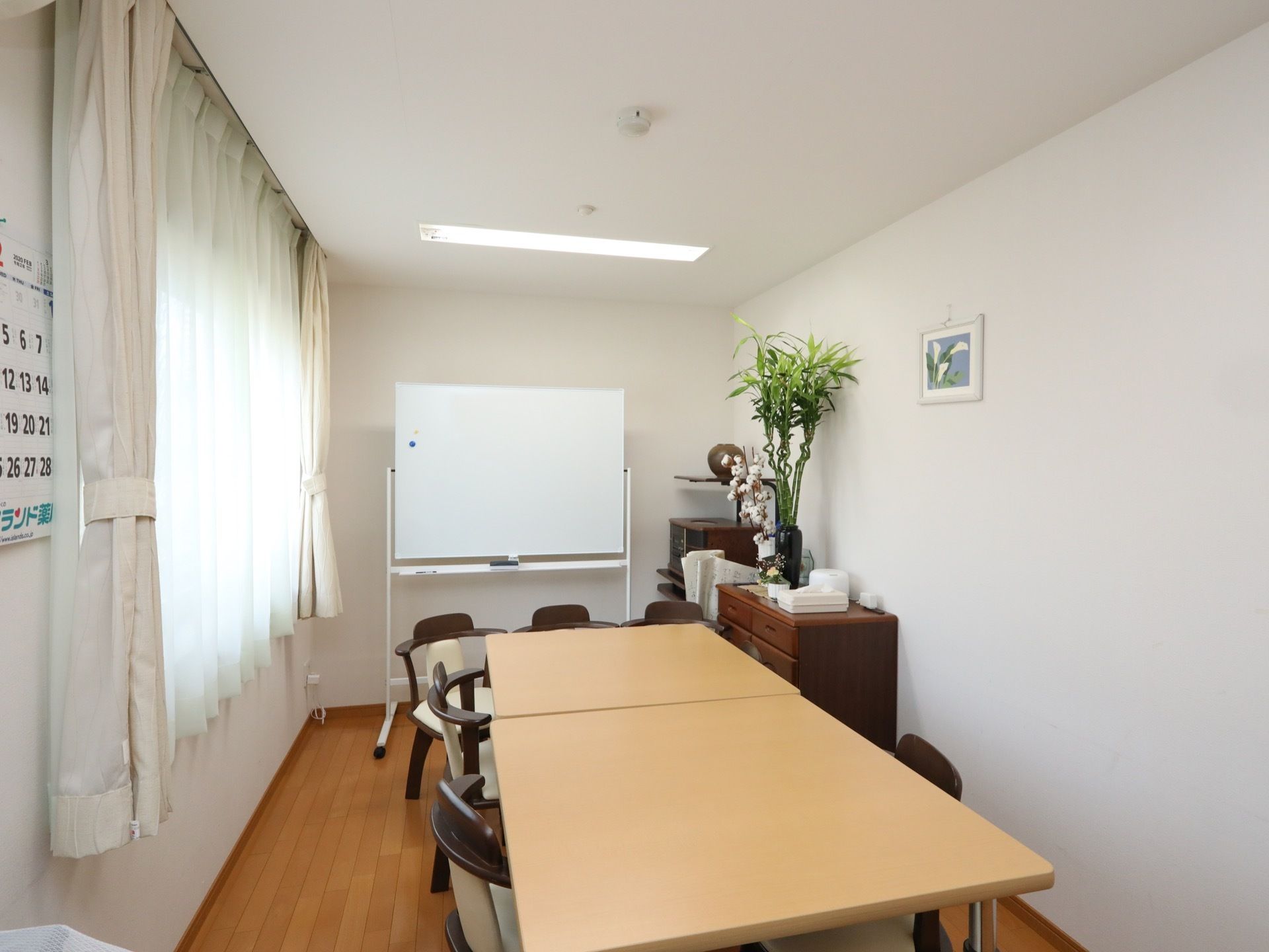 談話室の中央にテーブルが２台置かれている。横幅のある窓はレースのカーテンが閉められている。ホワイトボードが前の方にある。