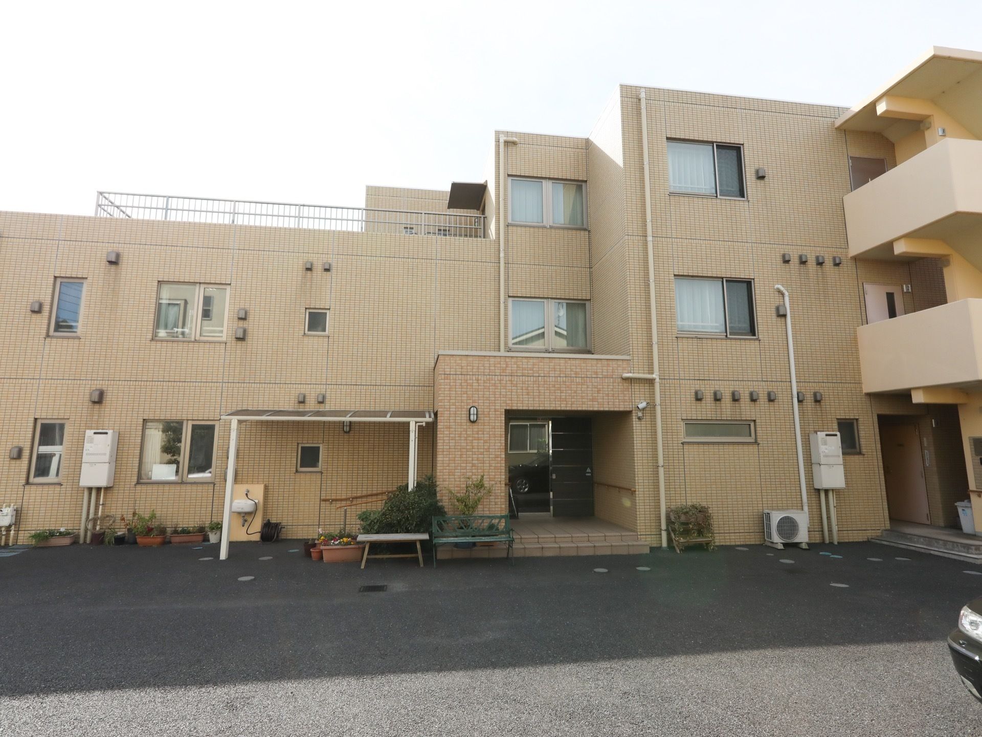 黄色系統の外壁の施設である。玄関の左側にあるスロープの上には屋根があり、その前にはプランターが置かれている。