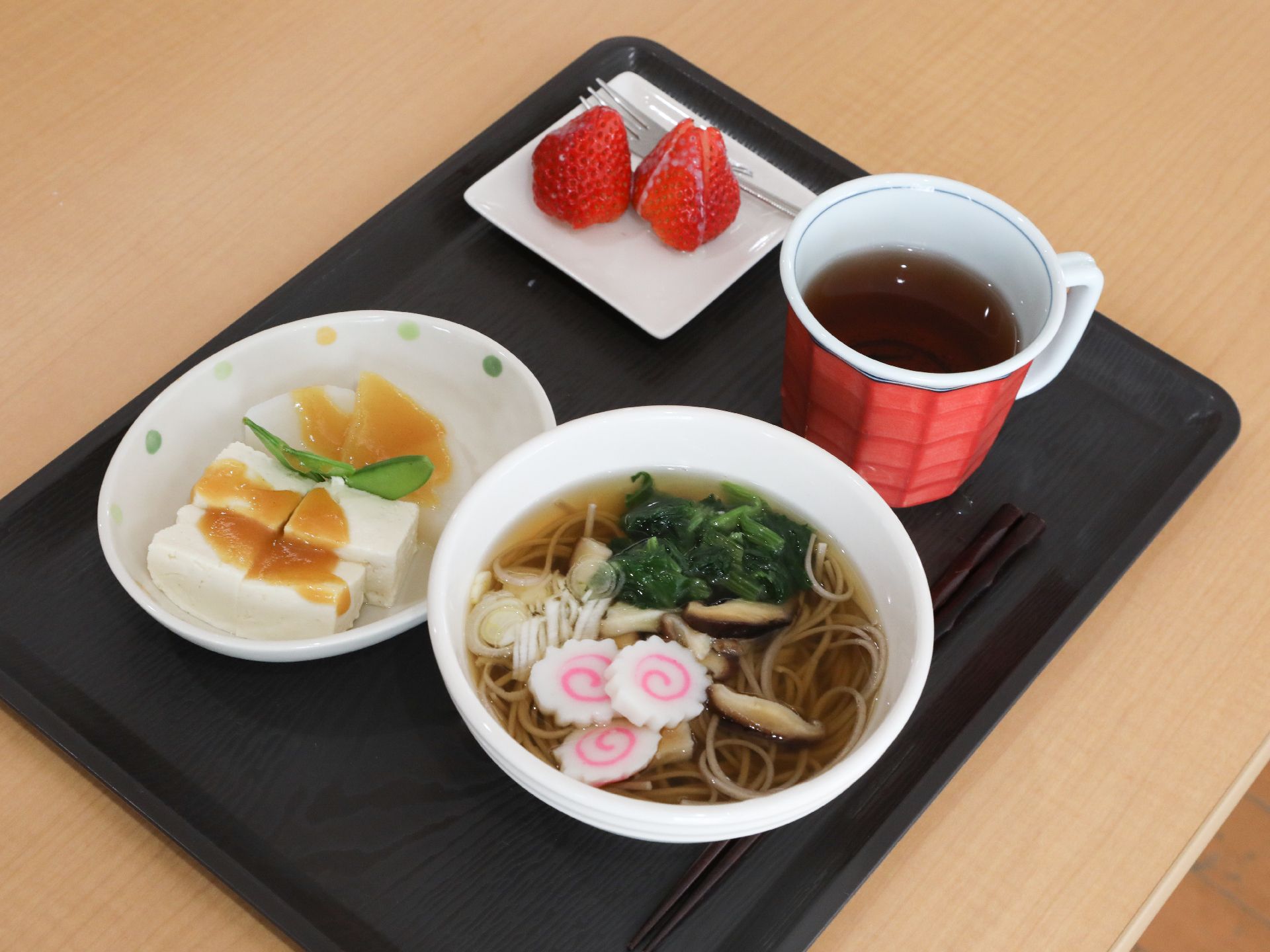 ラーメン、ごま豆腐、コンデンスミルクがかけられたいちご、お茶が配膳されたお盆