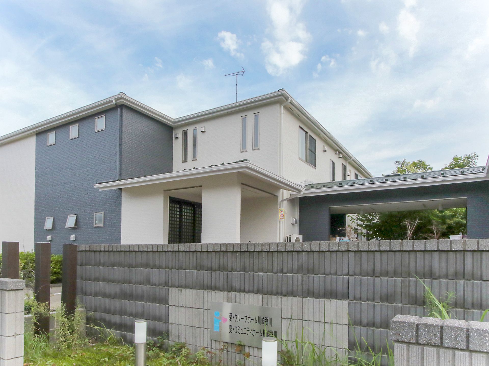 ブロック塀の奥に立地している白と黒の外観で２階建ての建物