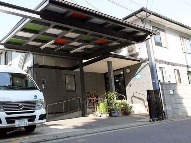 駐車場が付いた2階建ての建物には階段とスロープ付きの玄関がある。