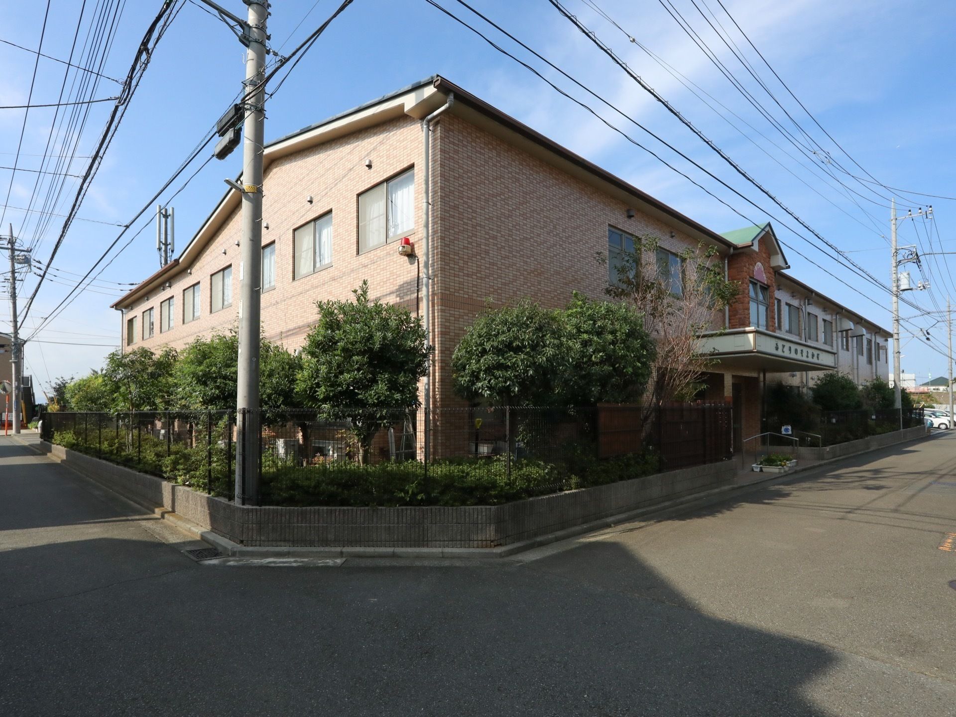 道路に面したところにレンガ調の２階建ての施設が建てられている。施設を囲むように樹々が植えられている。