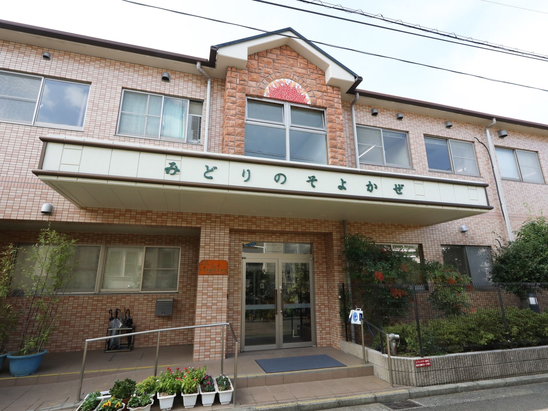 玄関には屋根が設置され、屋根の部分に施設名が書かれている。タイル張りの階段、スロープがあり、滑り止めのマットが敷かれている。