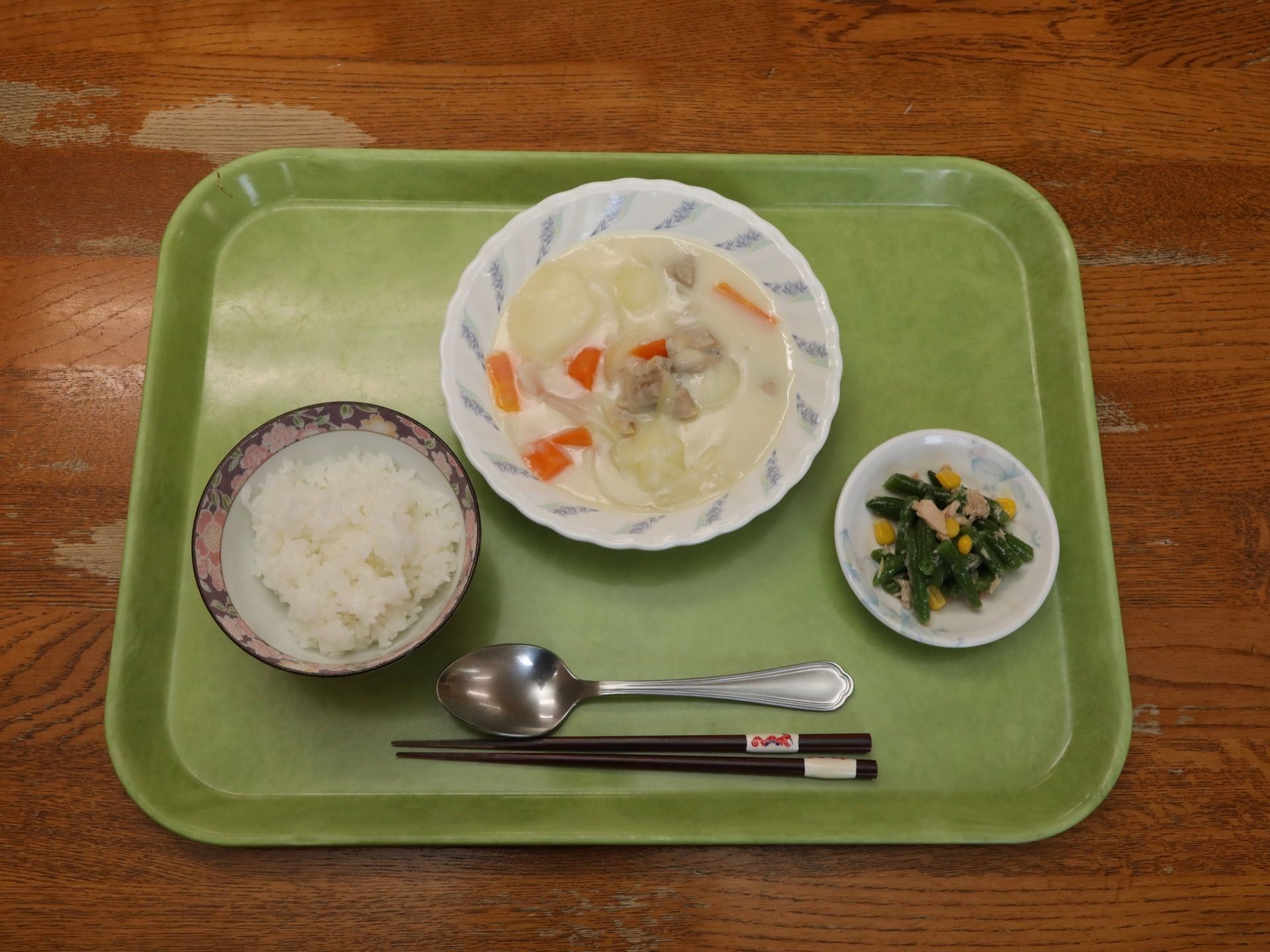 緑のおぼんに、鶏肉、じゃがいも、にんじん、玉ねぎが入ったクリームシチュー、ごはん、ほうれん草とコーンなどが和えられた副菜が並べられている。