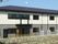 ２階建てのすっきりとした建物。上半分が白、下半分がグレー。菜園スペースもある。