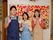 大きな作品が貼られた壁の前に、エプロンを掛けた３人のスタッフが笑顔で立っている。壁は白色で手すりが取りつけられている。