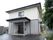 ２階建ての建物で、玄関の上には大きなひさしがついている。ドアの左側には傘立てがあり、壁にはインターホンや郵便受けが設置されている。