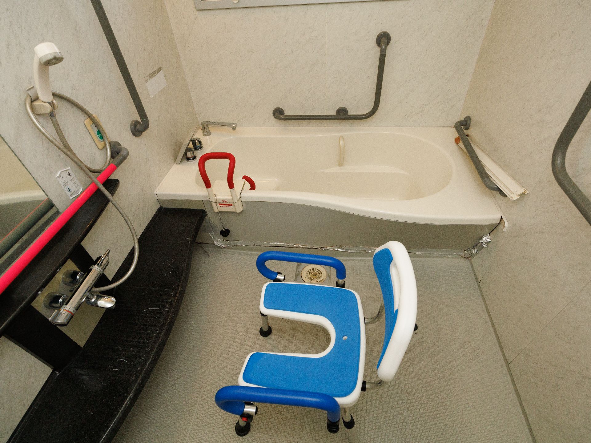 様々な手すりが壁についたシャワーチェアーのある浴室