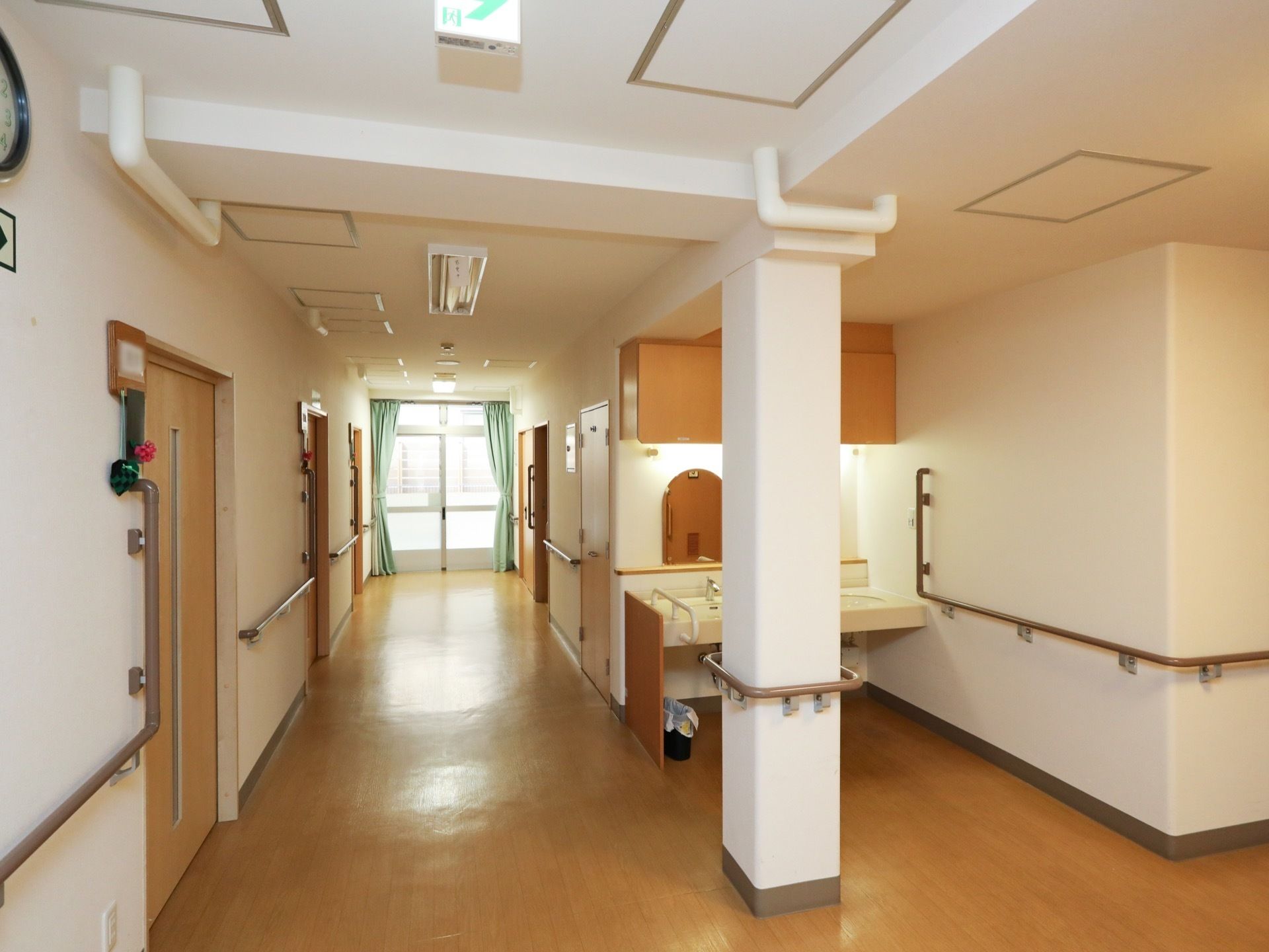 通路の壁伝いに、手すりが備えられている。突き当りに広々とした窓が設置され、自然光が入り込み明るい。