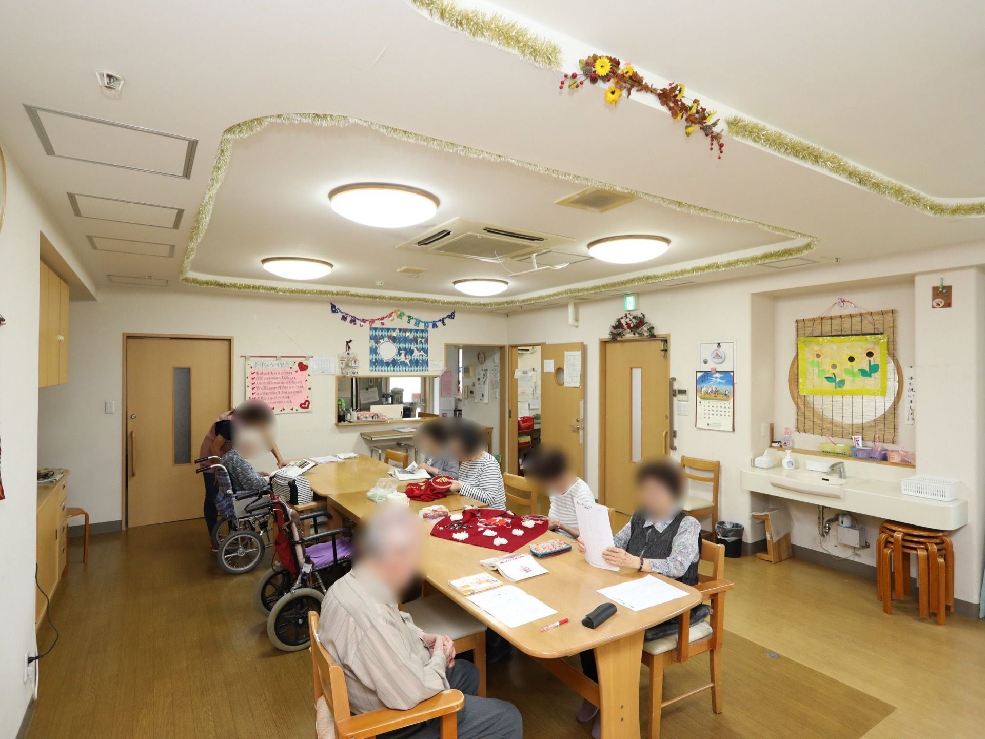 広々としたテーブル席に、複数人の入居者様が座り、思い思いの時間を過ごしている。天井には空調機がある。