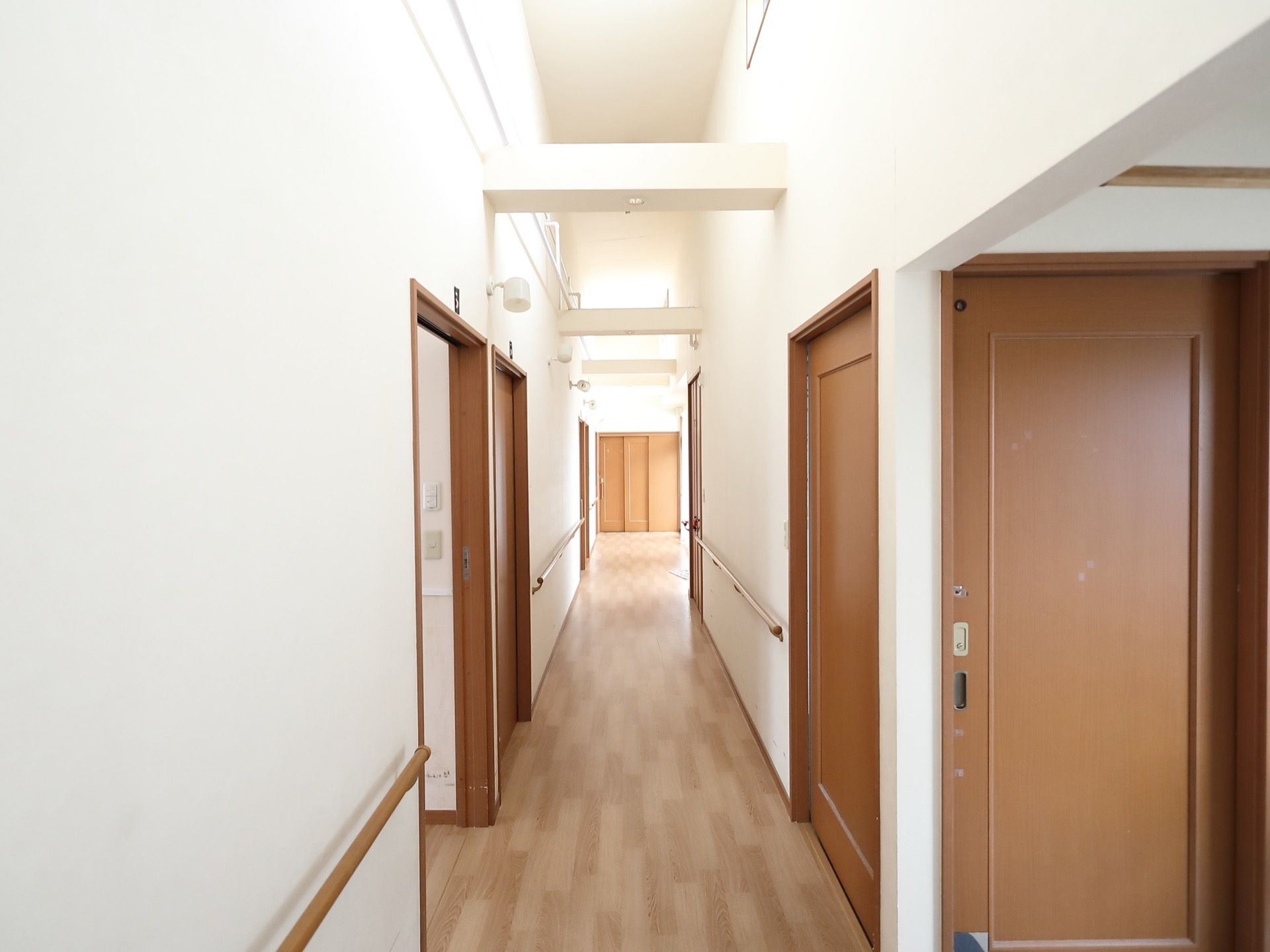 天井が高く吹き抜けになった廊下で、ところどころに梁が渡されている。突き当りには扉が３枚ある引き戸が見えている。