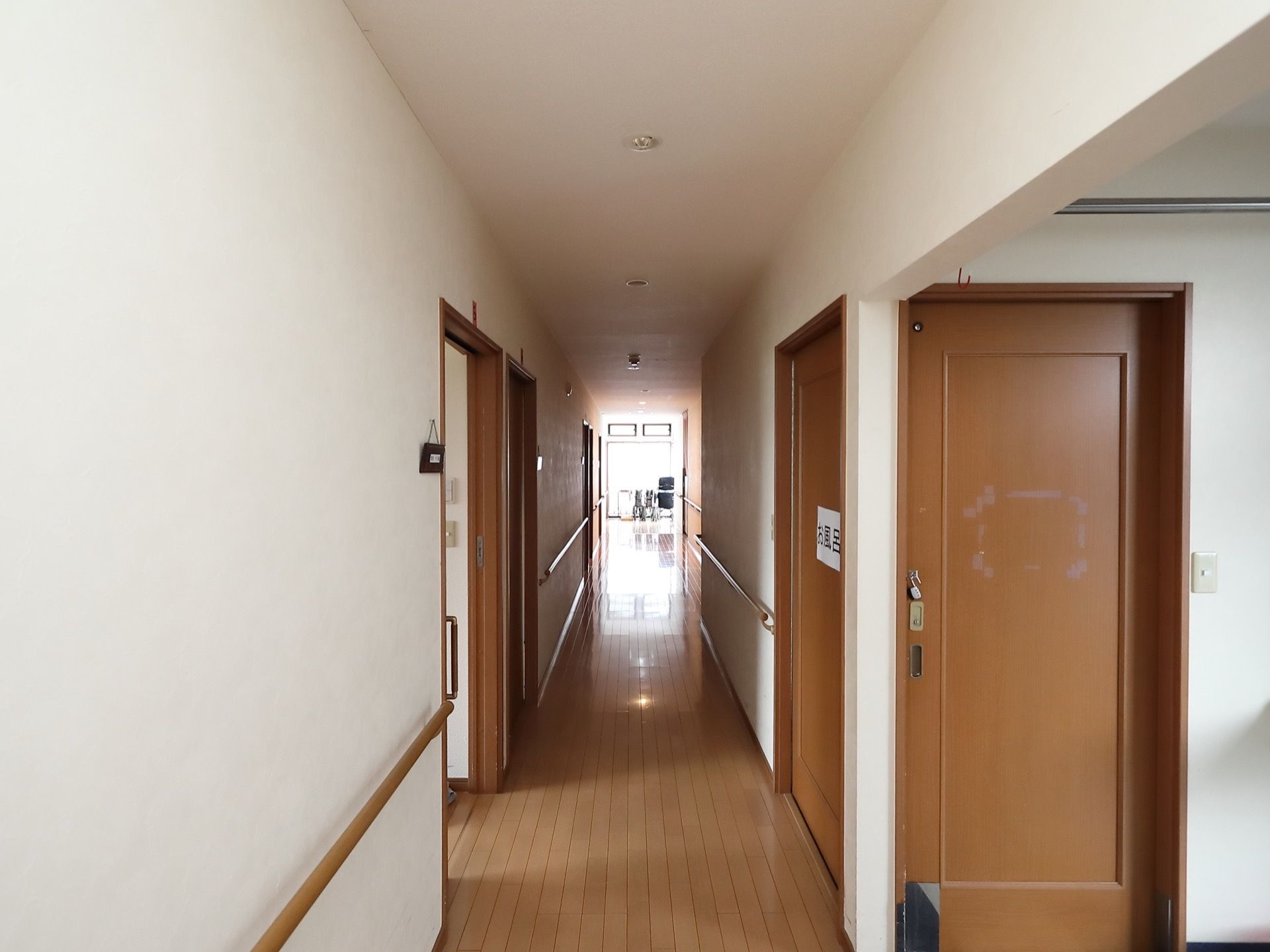 廊下の突き当たりにある大きな窓から外光が差し込んでいる。壁には木製のドアが取りつけられ、右手に浴室へのドアがある。