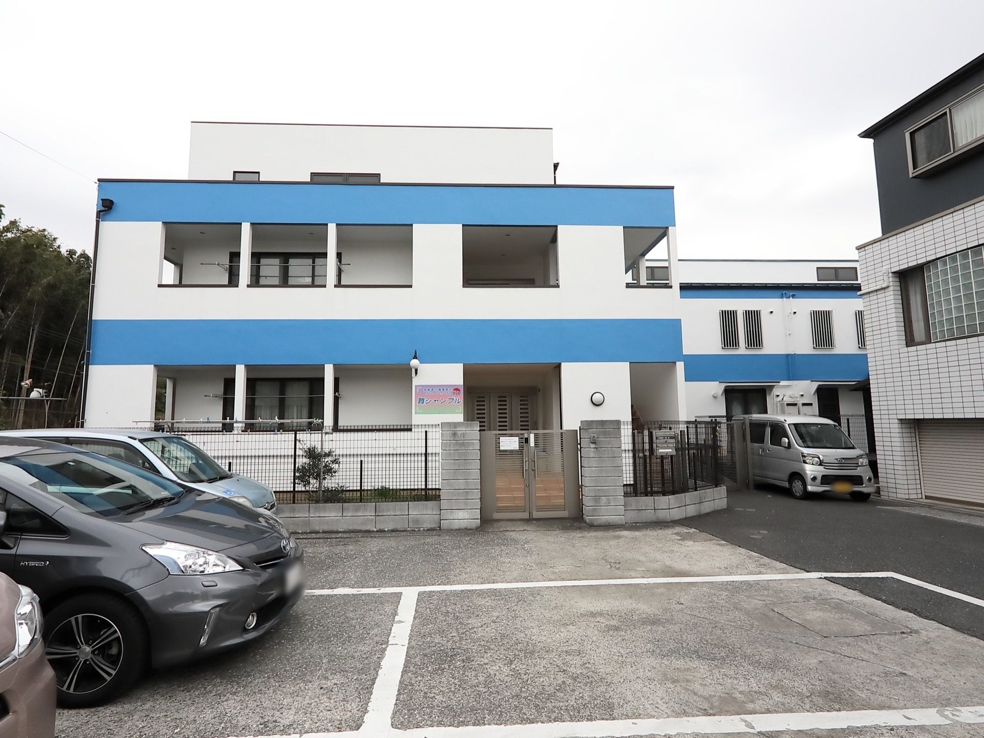 水色のラインが入った白メインの施設である。施設周りはフェンスで囲まれており、門がある。施設前は駐車場になっている。