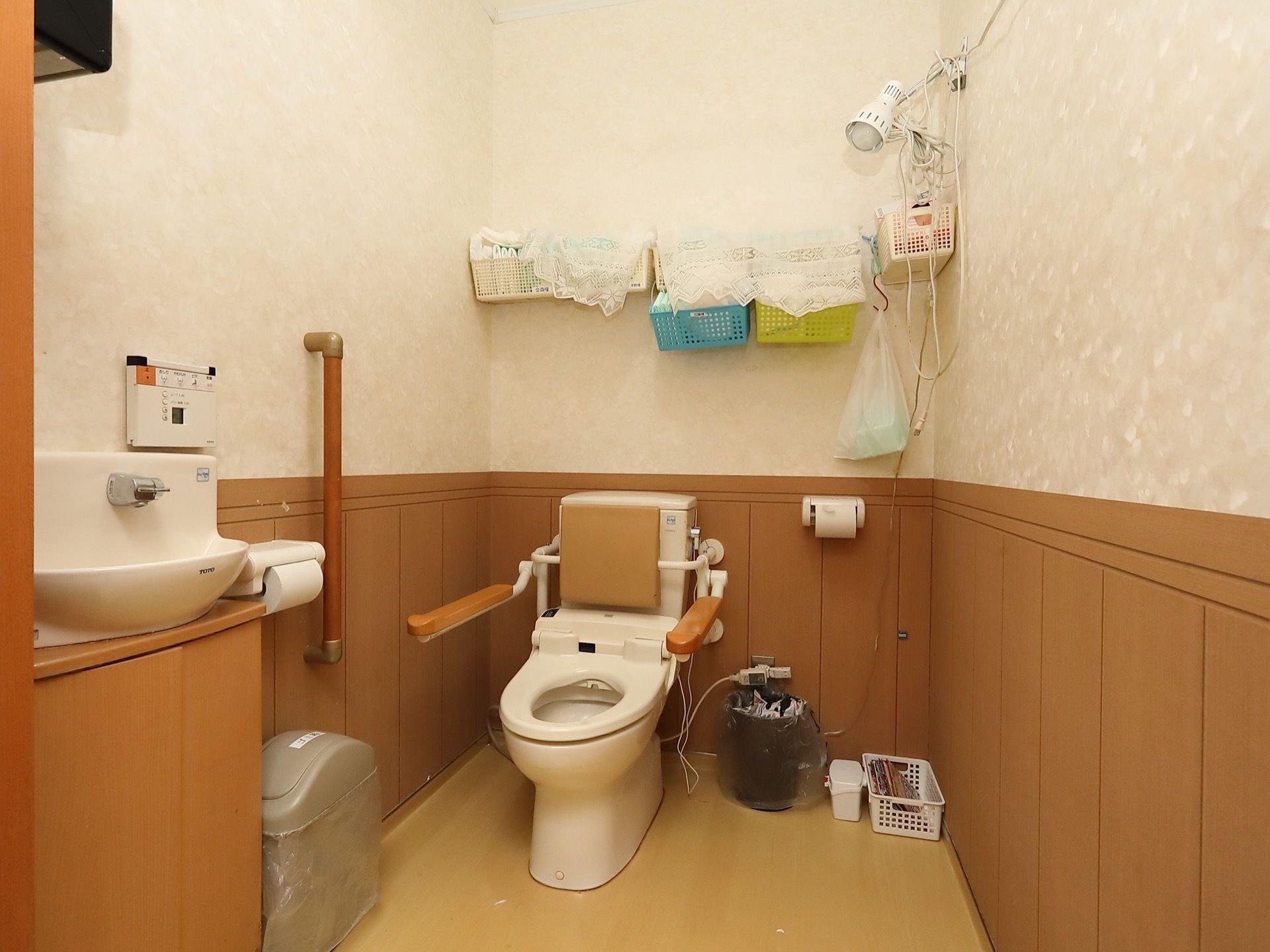 板張りを模した腰壁が施されたトイレスペースに、洋式便器が設置されている。壁面に複数の小さな収納カゴがある。