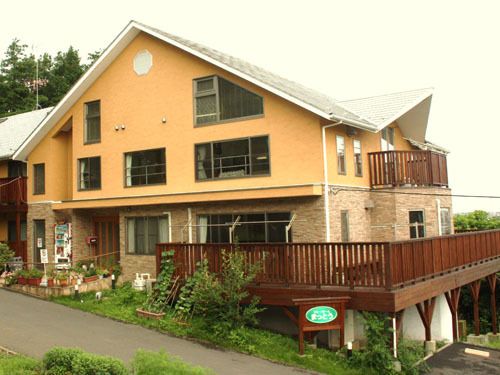 右側は屋根が高く、左側にはベランダが連続している。アスファルトで舗装された部分に、野外用の椅子やテーブルがある。