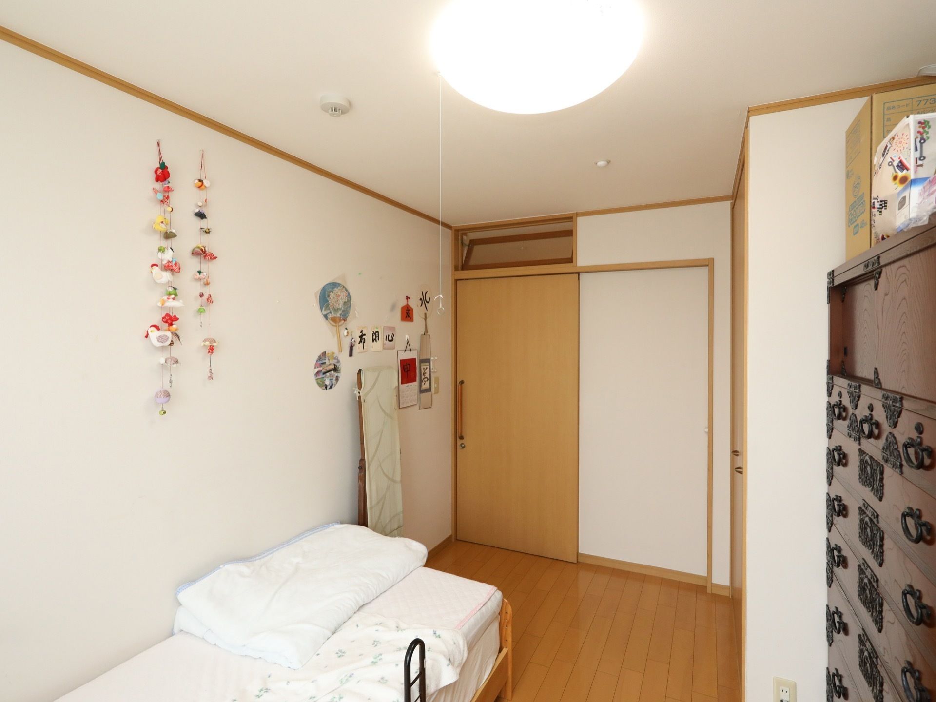 親しみやすい、落ち着いた色合いの洋室である。扉は引き戸式。壁側にベッドがある。整理ダンスもある。
