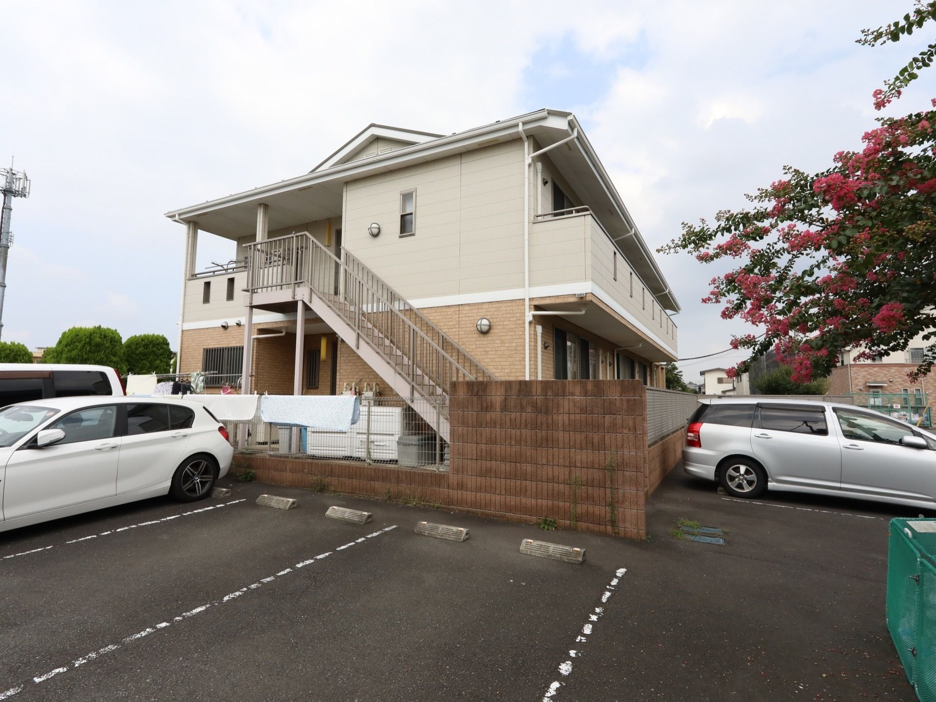 明るい色合いに施された、２階建ての施設である。非常階段がある。敷地はアスファルト路面。駐車場も完備されている。