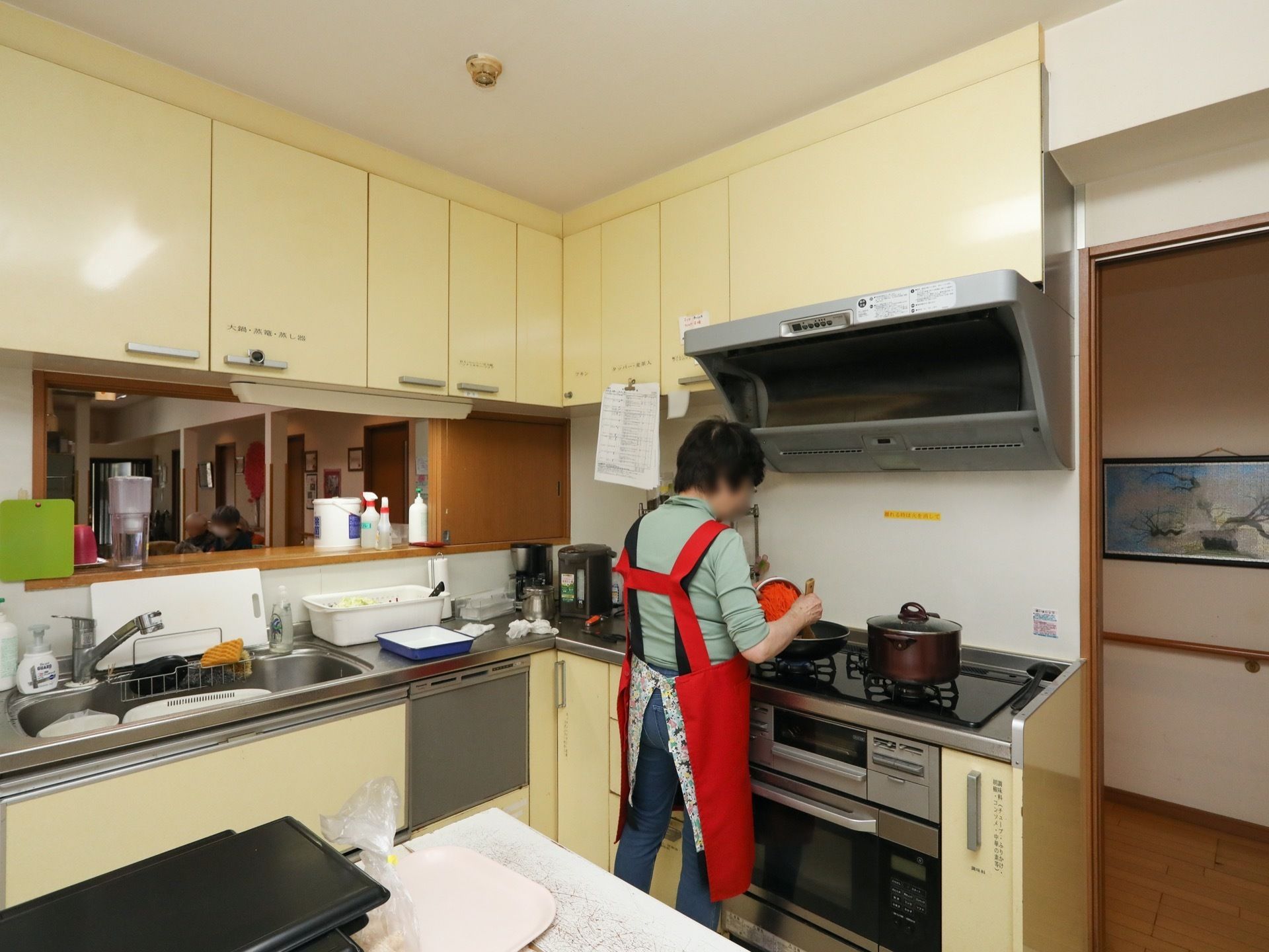 キッチンで赤色のエプロンをした女性スタッフが調理をしている。その上には大きなレンジフードが設置されている。