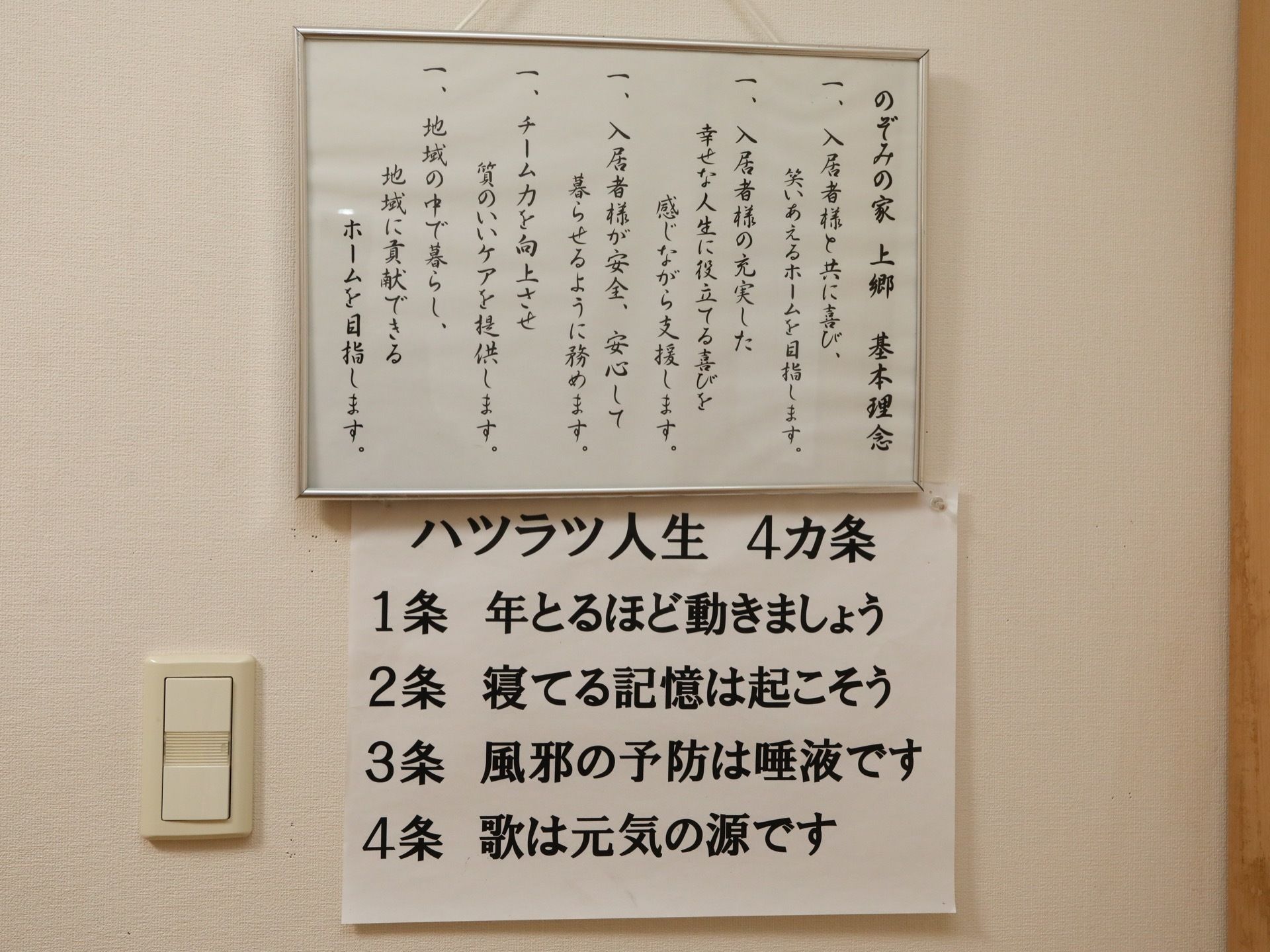 白い壁に施設の基本理念が筆で５つ書かれた額縁と、ハツラツ人生についての４か条が書かれた紙が掲示されている。