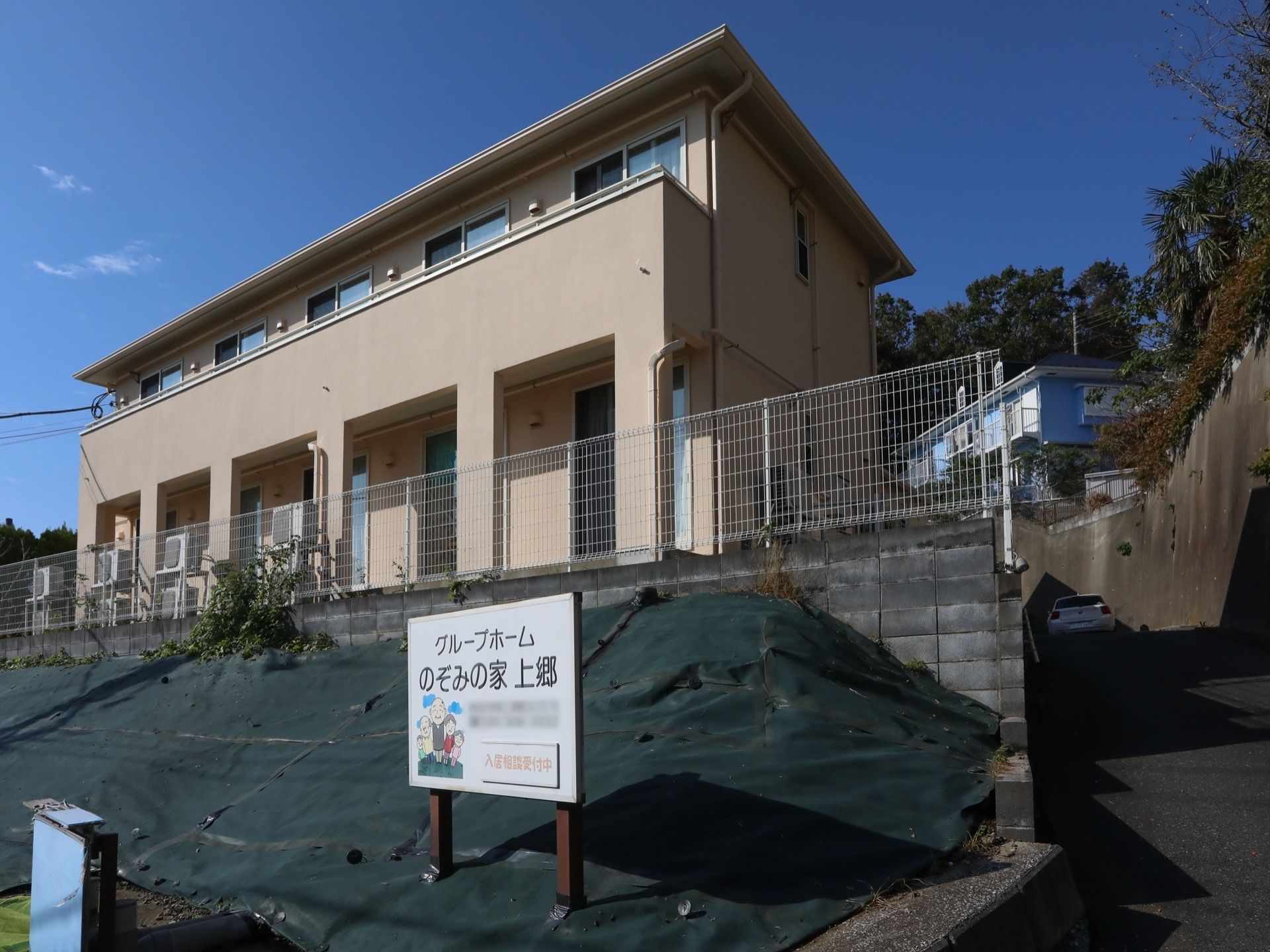ベージュを基調とした２階建ての施設。施設の周囲は白い柵で囲まれ、２階部分にベランダが設置されている。