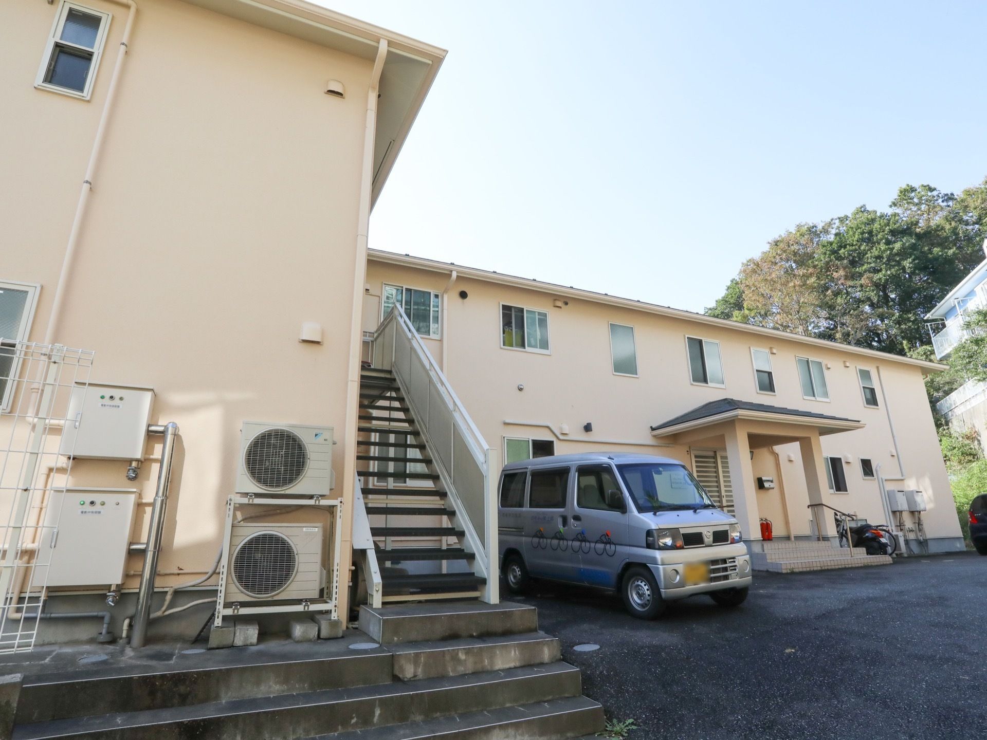 ２階建ての施設はL字型になっており、2階から駐車場へ通じる非常用階段が設置されている。駐車場には車がとめられている。