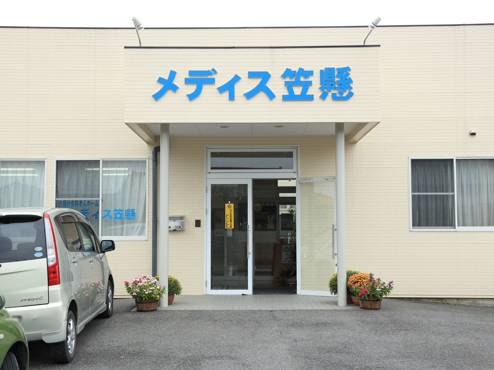 施設名が玄関の屋根に水色で大きく書かれている。入口付近には色鮮やかな花が咲き乱れ美しい。また、バリアフリー構造で安心。
