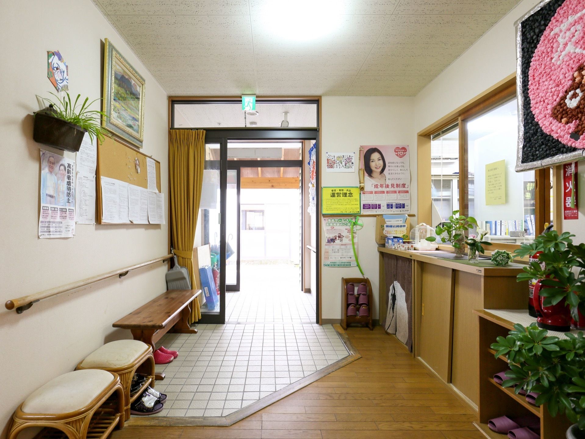 館内から玄関を見た図である。ガラスの片開き扉が開けられている。左手の壁際に長椅子や椅子が置かれている。