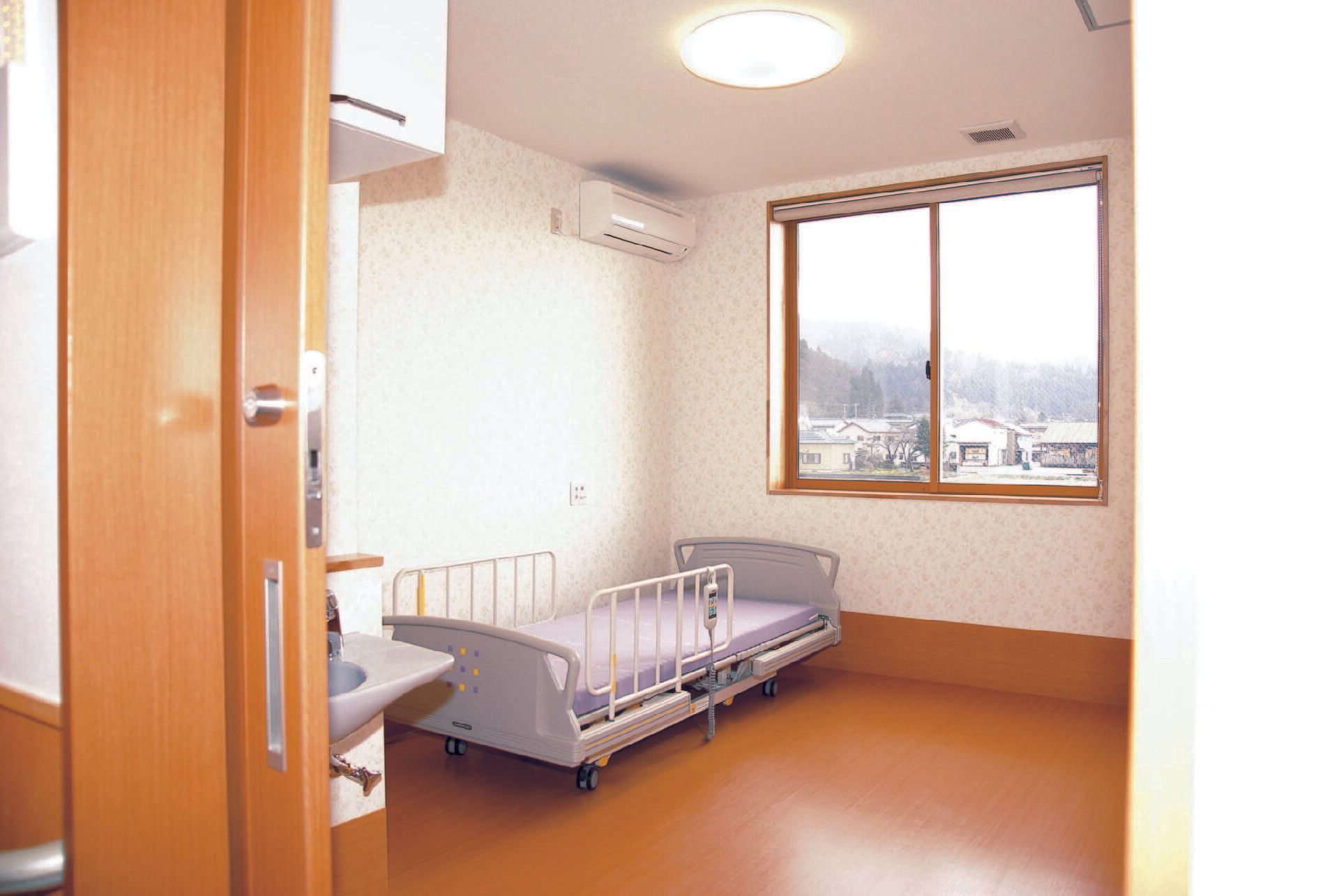介護ベッドやエアコン、洗面所があるフローリングの部屋にはカーテンのない大きな窓があり、スライド式のドアが設置されている。