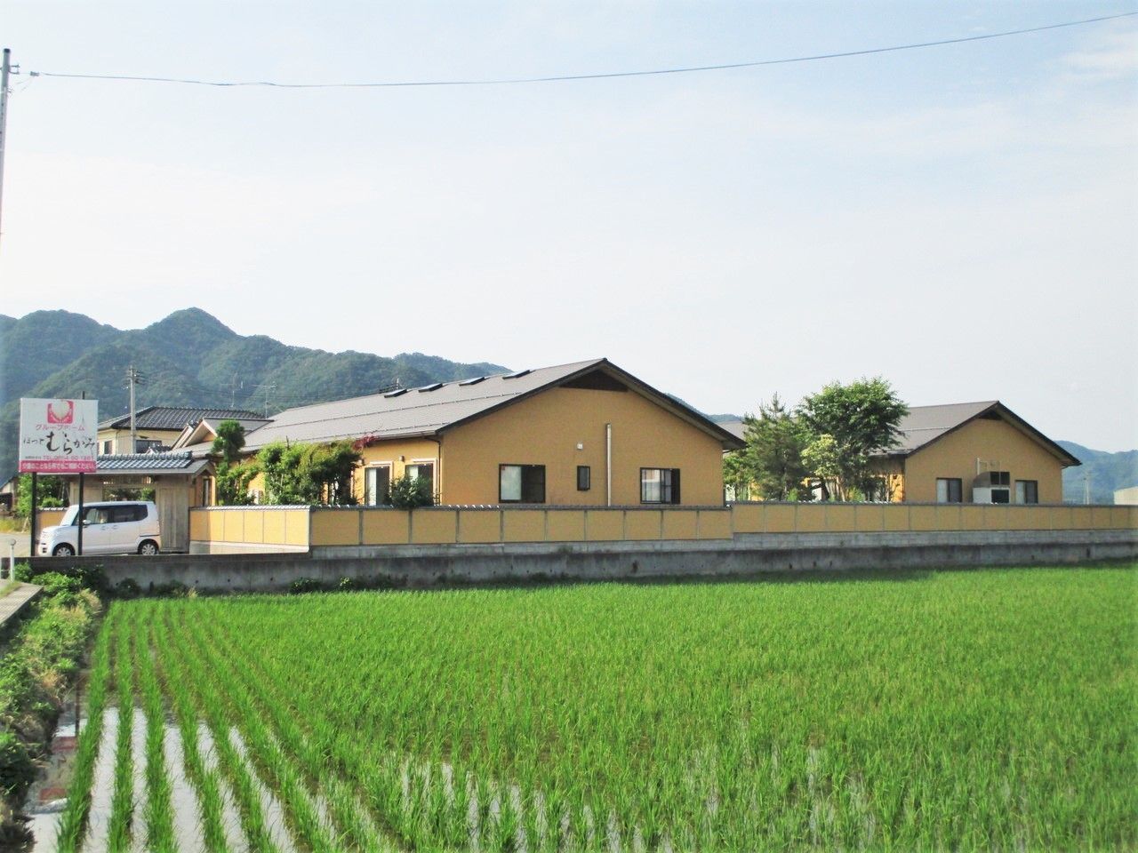 てまえに広い田んぼが写っている施設の周辺。建物の奥は山に囲まれている様子