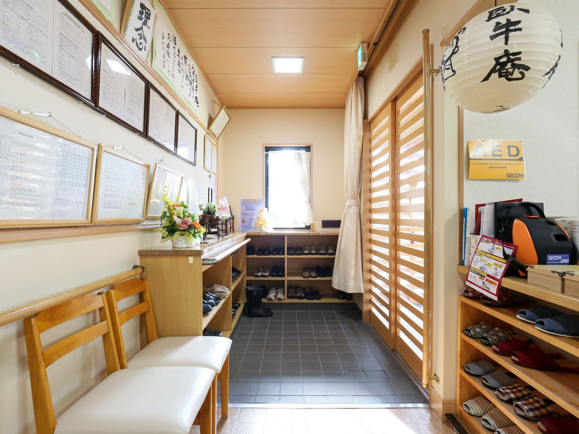 入り口扉は木製の引き戸が閉められている。向かって左側の壁には、たくさんの額縁がかけられ、その下に下駄箱がある。