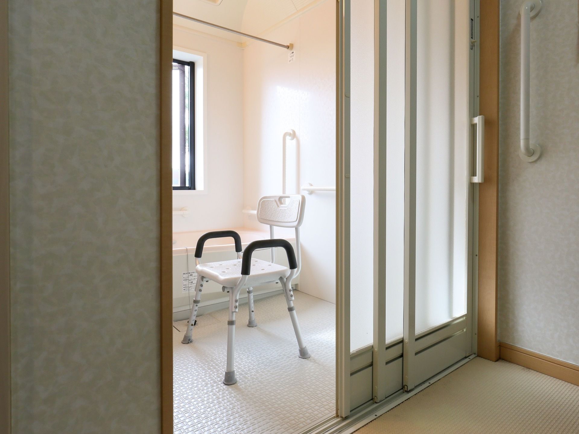 脱衣所から個浴用浴室の内部を見た図である。白い引き戸が開けられており、中には浴槽と椅子が１脚置かれている。
