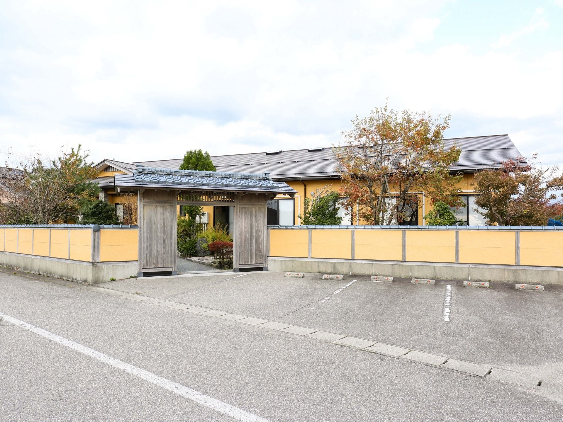 奥にオレンジ色の壁の建物があり、同じ色のフェンスで囲まれている。施設の前は駐車場と道路が広がっている。