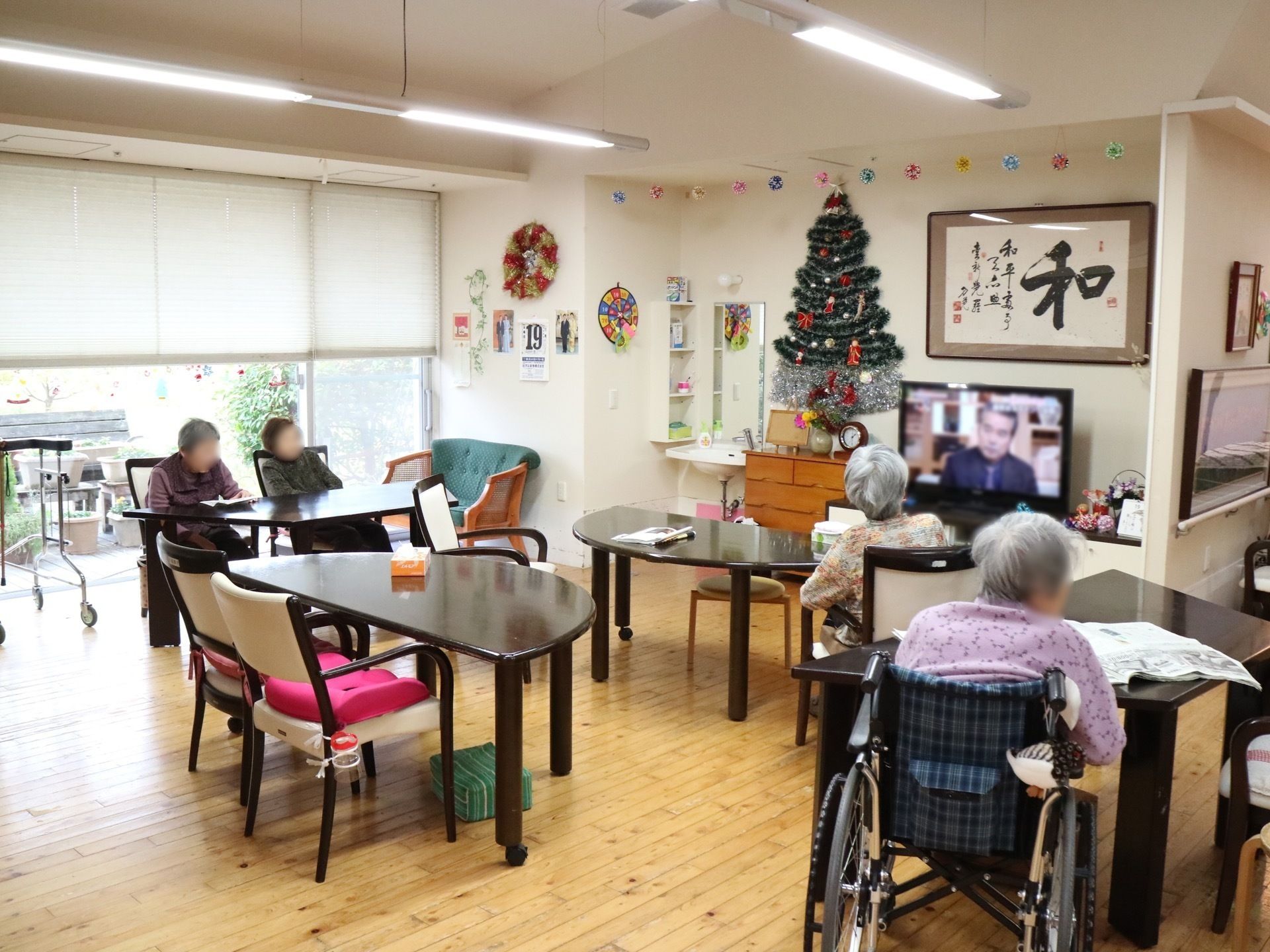 共有スペースで、テレビや新聞を見ている四人の高齢者
